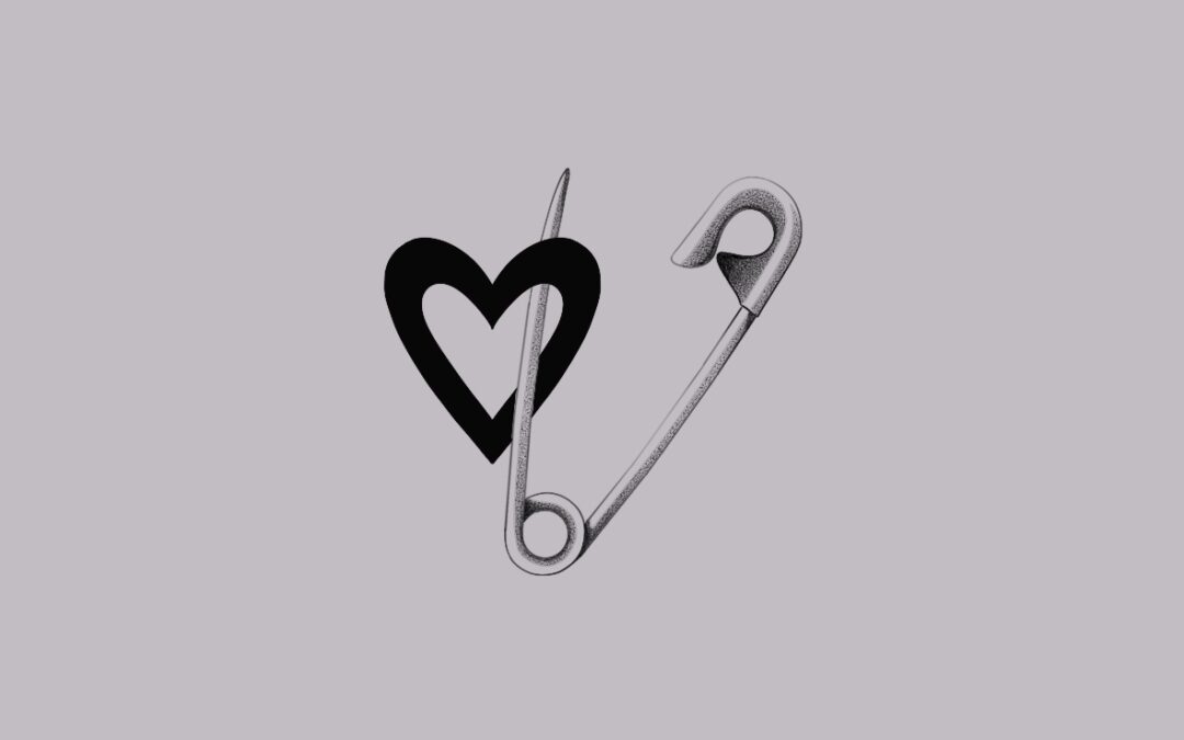 A small delicate tattoo desing of a safety pin and a heart